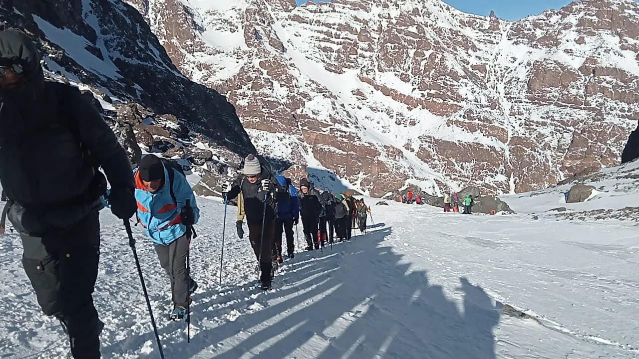 Des randonneurs avancent en file sur la neige, au pied de parois rocheuses striées de neige